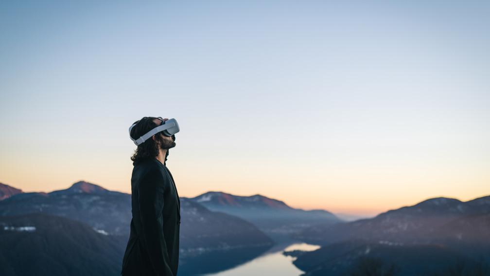 Person mit Virtual Reality Brille schaut ins Weite Hintergrund See und Gebirge