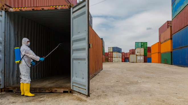 Mann in Schutzanzug desinfiziert einen Gütercontainer